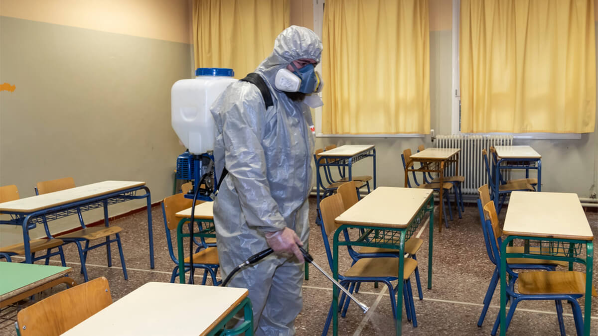 Man in protective suit sprays empty school classroom with disinfectant